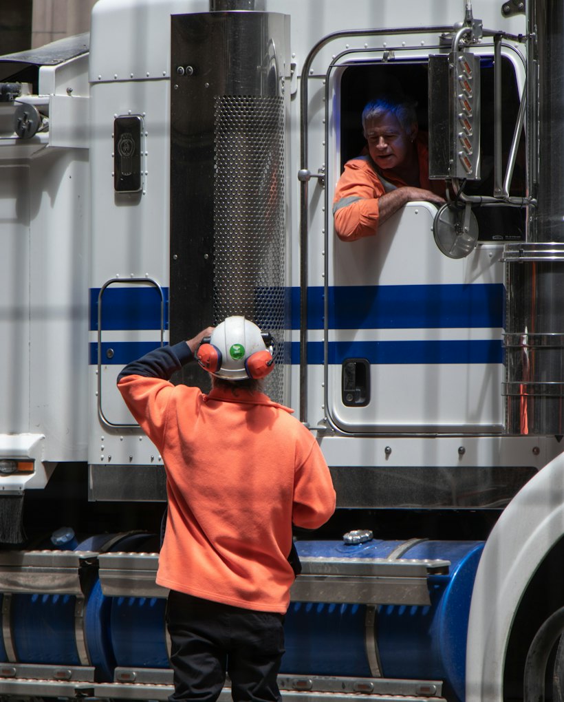 Truck driver leaning out of the cab window talking to a yard worker in a high-visibility jacket